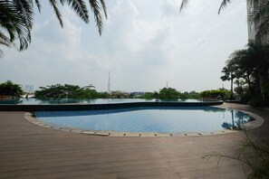 Una piscina con muelle de madera, rodeada de palmeras y follaje.