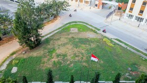 A grassy area with a flag, a road, and buildings in the background. - Comfy Studio Mustika Golf Apartment (Cikarang)
