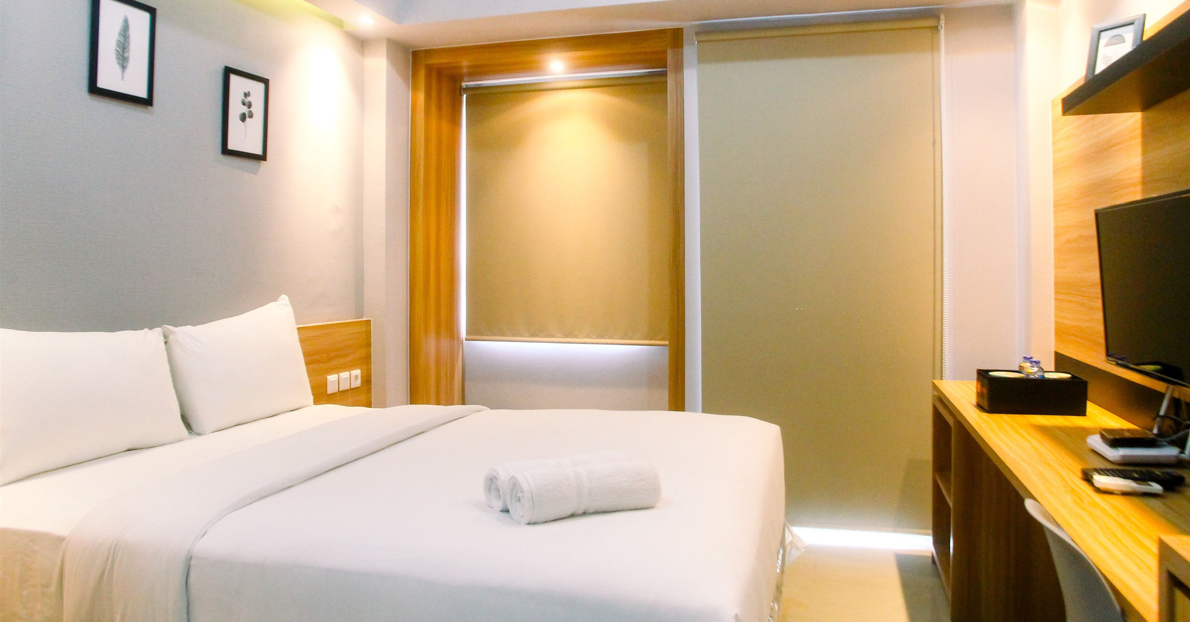 Una camera d'albergo con un letto rifatto, un comodino in legno con un telecomando, una televisione su un mobile in legno e un armadio con ante scorrevoli.