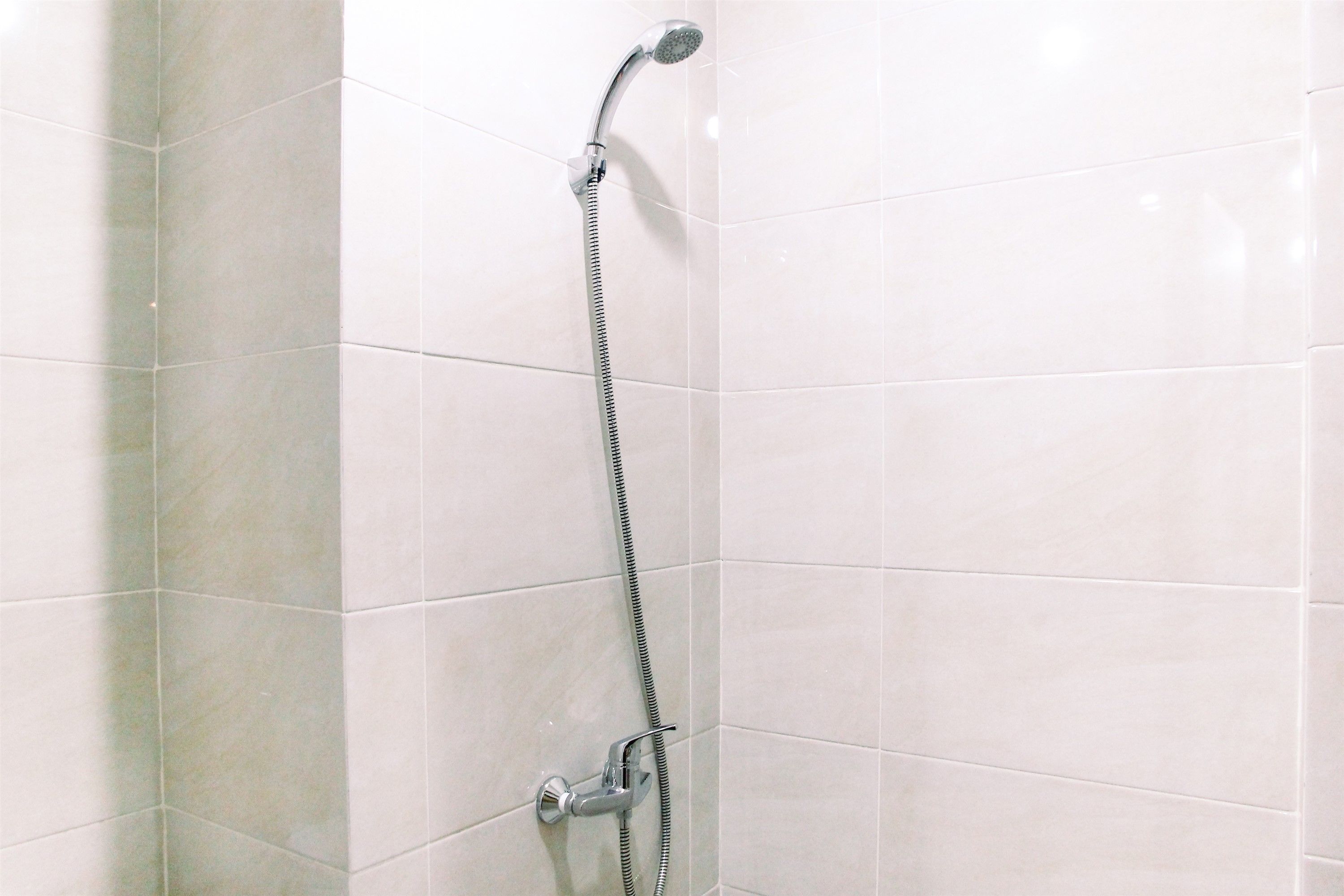A corner shower with a handheld showerhead and a fixed showerhead, mounted on a tiled wall.