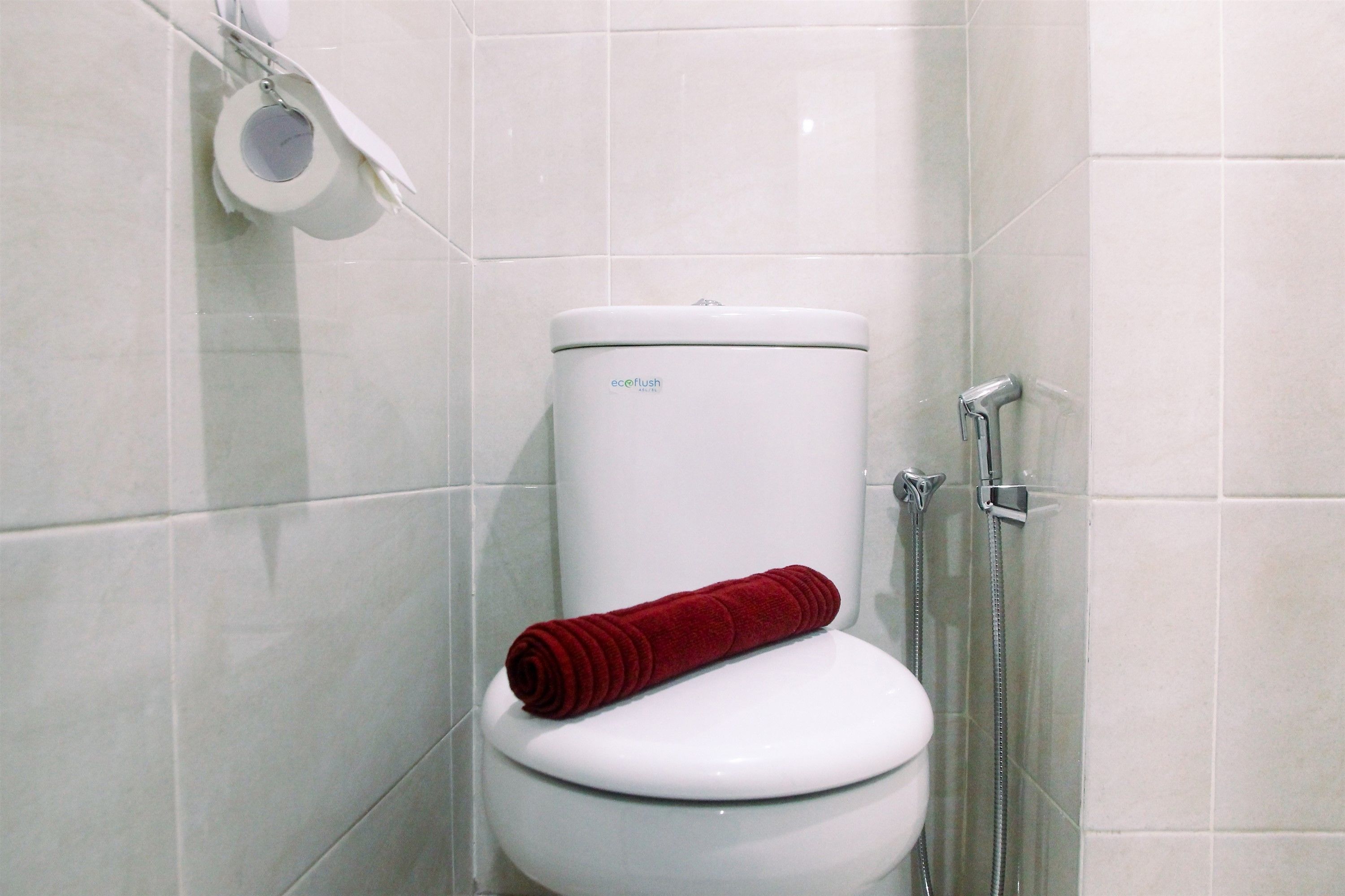 A white toilet with a red towel on the seat, a toilet paper holder, and a shower head.