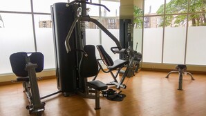 Een sportschool met diverse fitnessapparaten, grote ramen en een houten vloer.