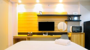 Hotelkamer met een bed, een flatscreen-tv, een magnetron, een klein tafeltje met een afstandsbediening en een wandplank met een fotolijst.