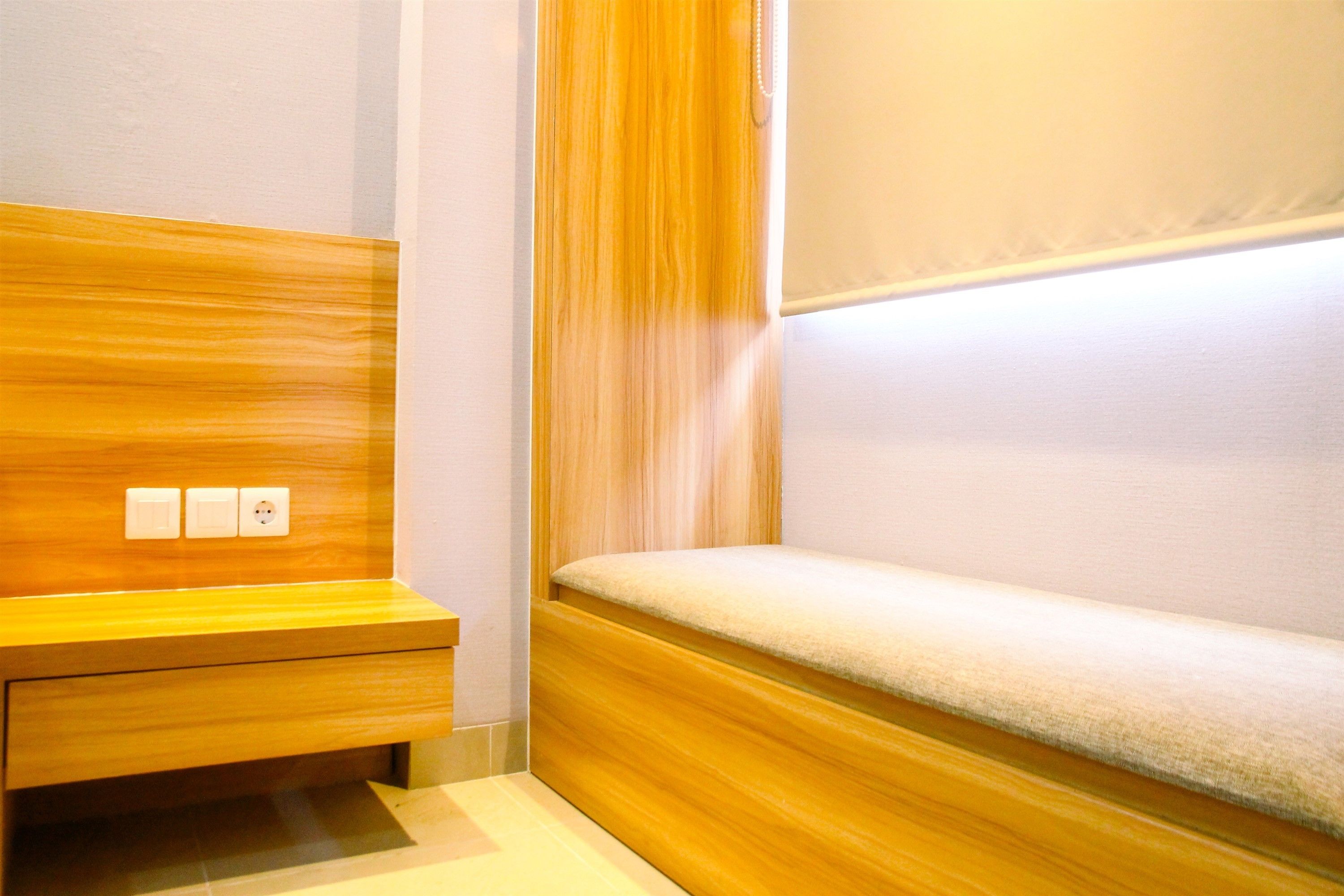 Un banco de madera con asiento acolchado y una lámpara fijada a la pared.