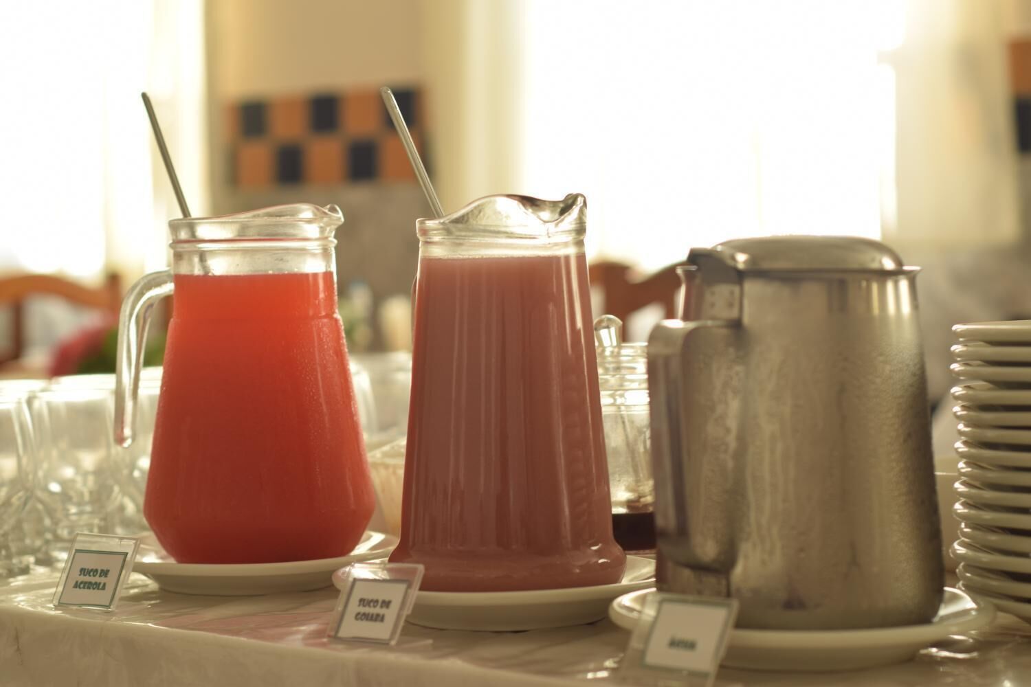 A buffet table with a pitcher of red juice, a pitcher of pink juice, and a metal pitcher, likely for coffee or tea.