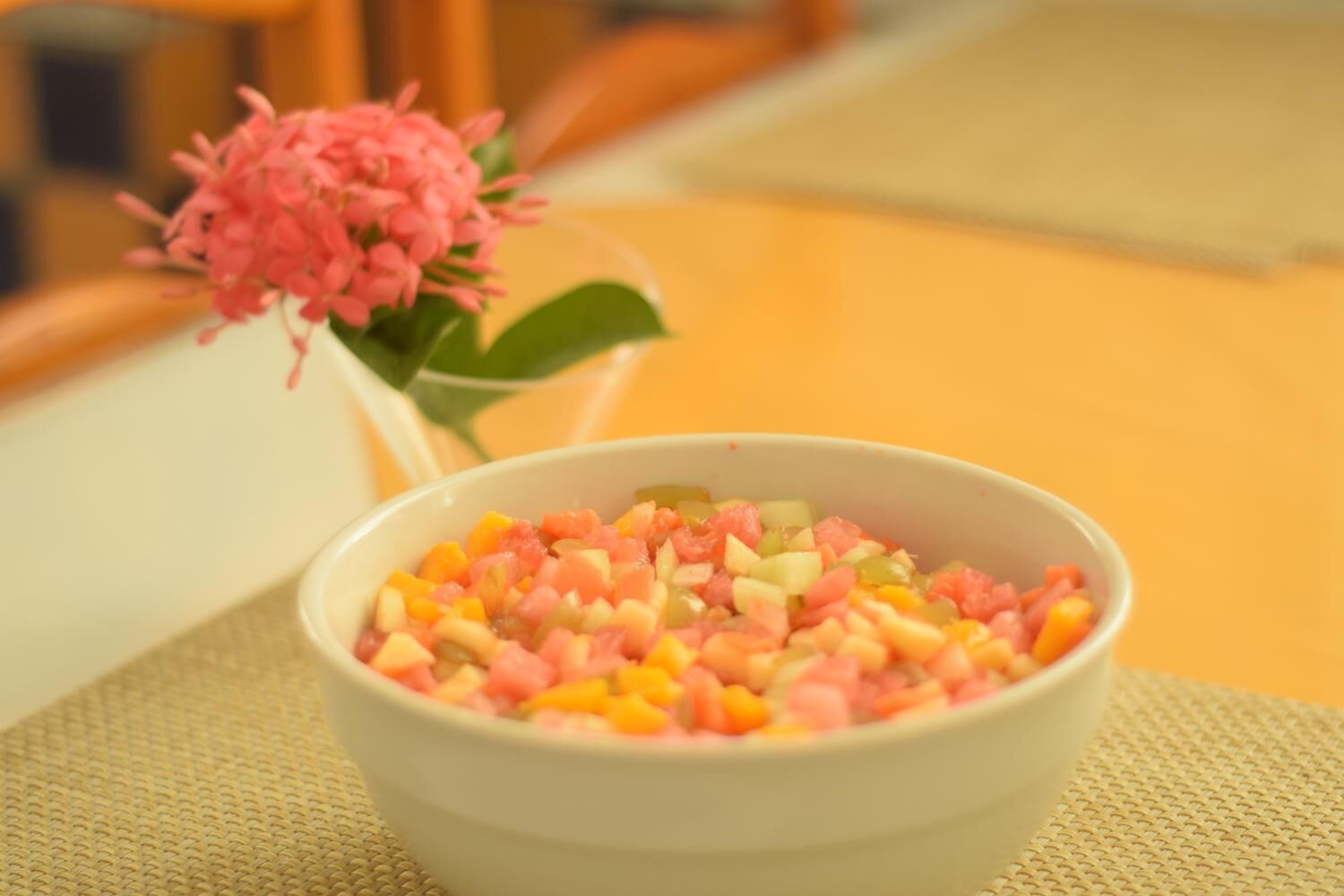 Un tazón de ensalada de frutas cortadas sobre una mesa con un posavasos tejido.