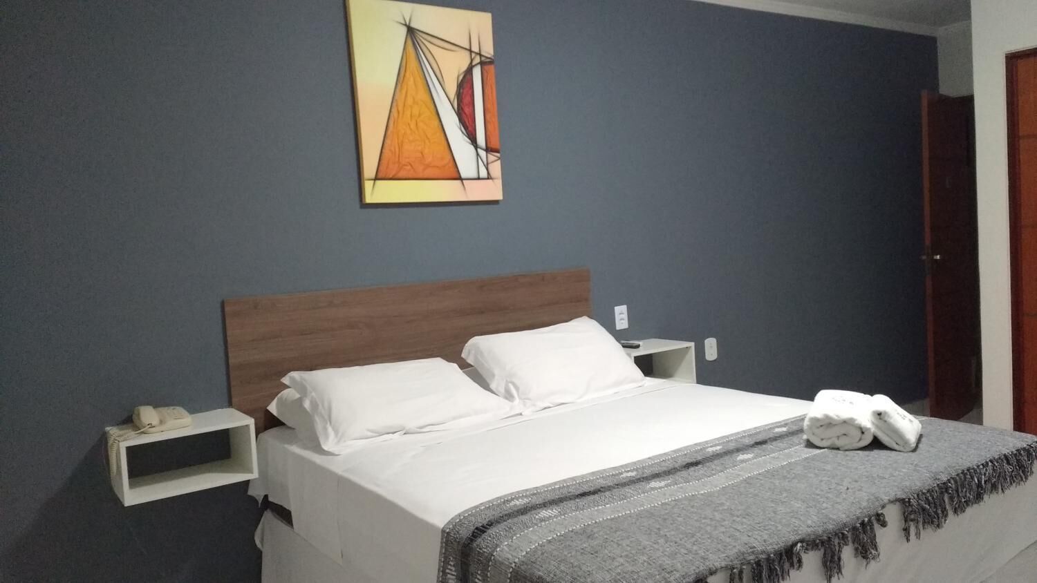 Una cama bien hecha con sábanas blancas, un plaid gris y una toalla blanca al lado.