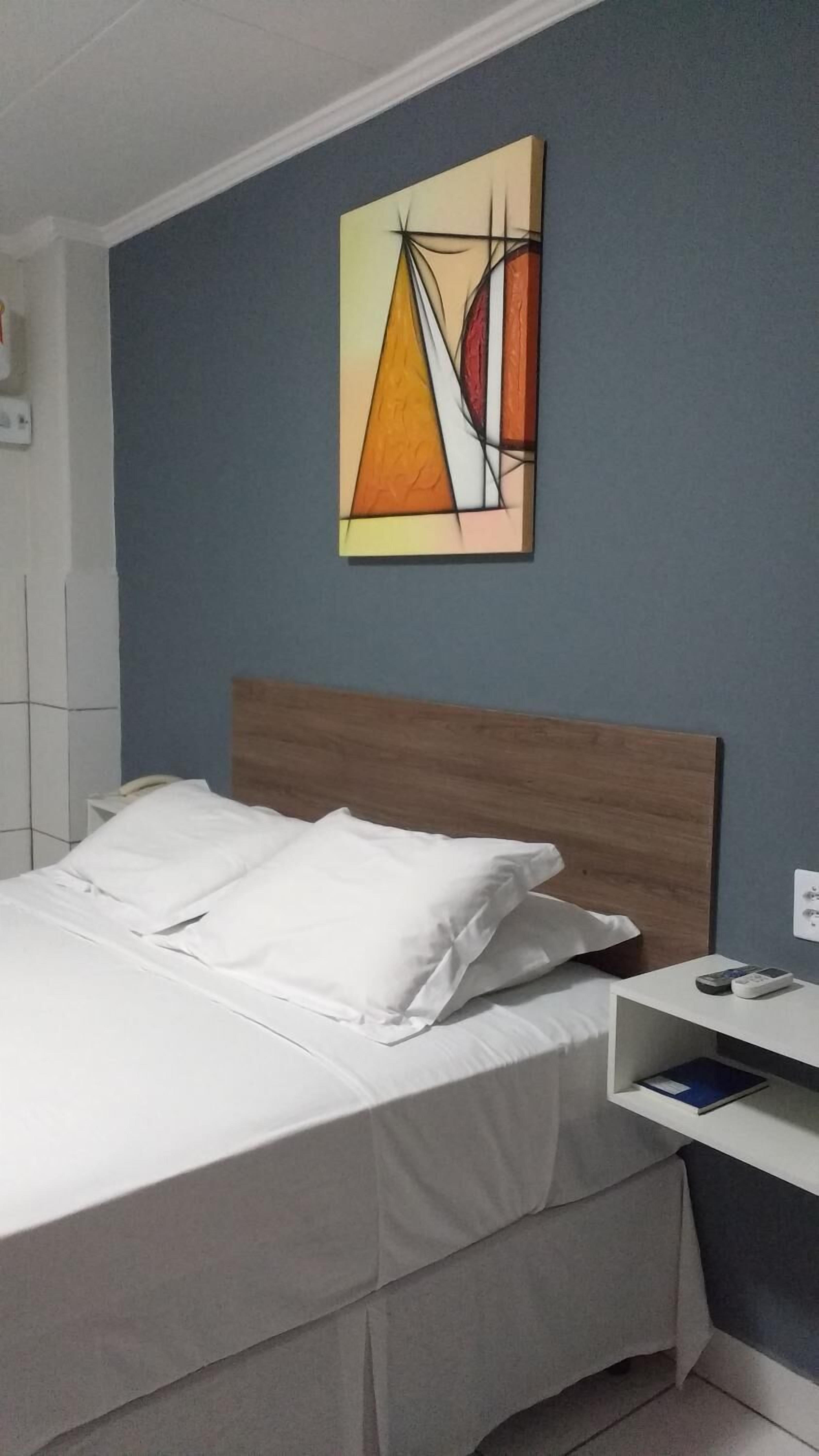 A neatly made bed with white linens in a room with a blue wall and a wooden headboard.