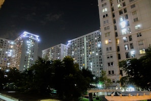A high-rise residential building with multiple floors, illuminated windows, and a well-maintained surrounding area with trees and a pathway.
