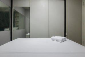 A hotel room with a neatly made bed, a wardrobe, and a mirror reflecting part of the room.