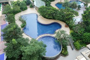 A rooftop pool area with multiple swimming pools surrounded by lush greenery and palm trees. - Comfy Studio Woodland Park Residence Apartment (Jakarta)