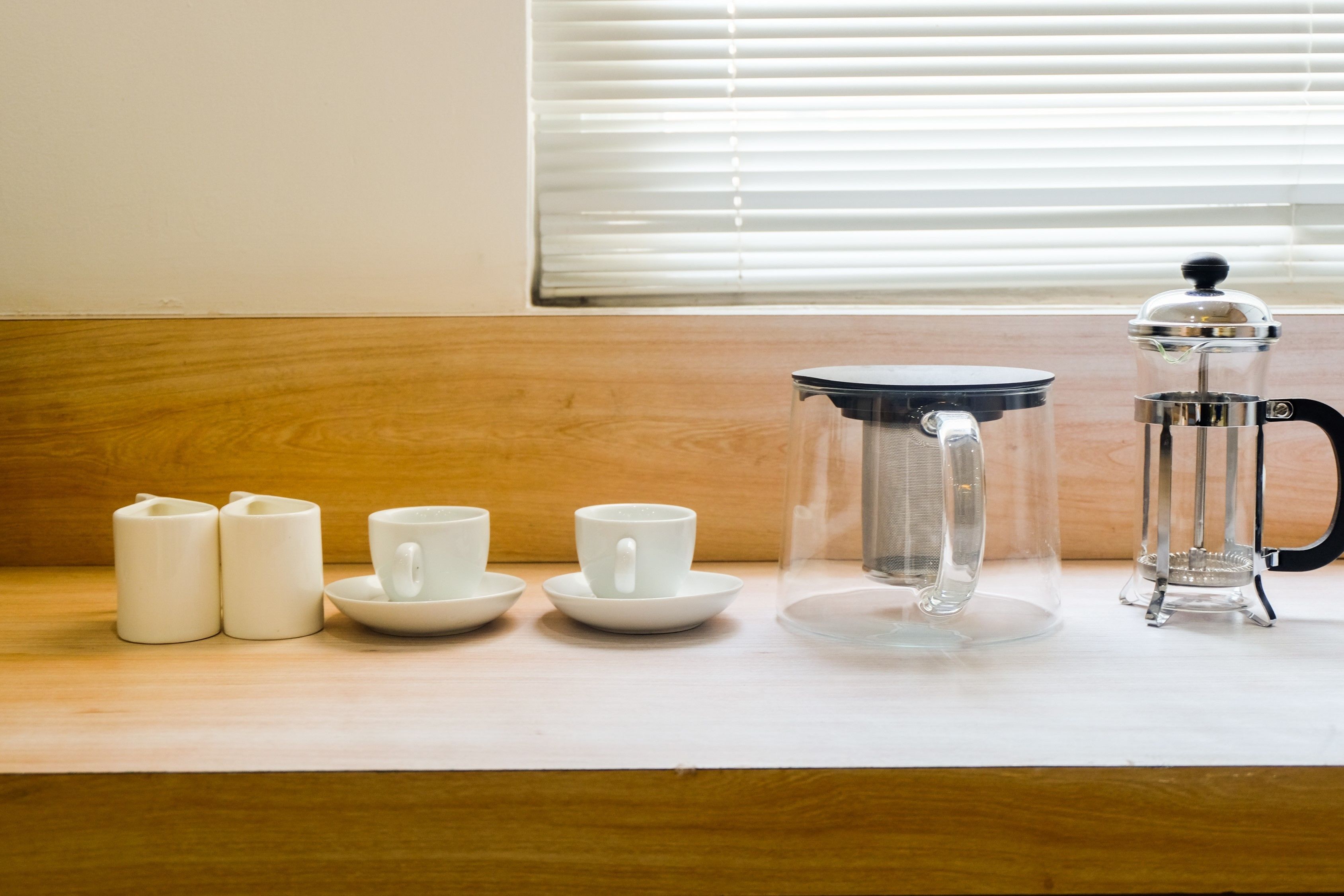 A kitchen counter with a coffee maker, two white mugs, and two white candle holders.
