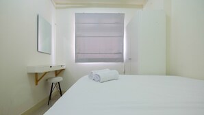 Ein Hotelzimmer mit einem Bett, einem kleinen Hocker, einem Schminktisch mit Spiegel und einem Fenster mit Jalousien.