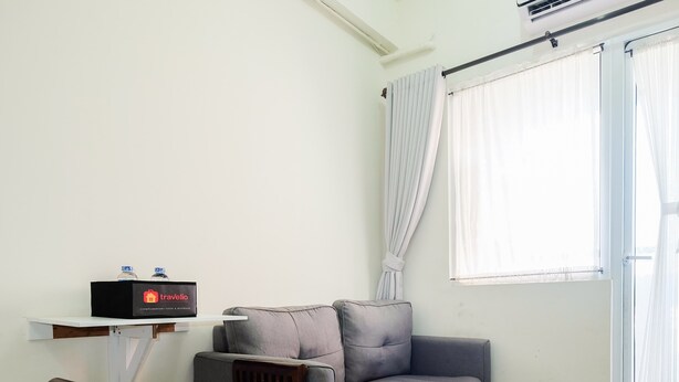 Una sala de estar con un sofá gris, una silla de madera, un tapete morado, un estante blanco con una botella de agua y un letrero de Travello.
