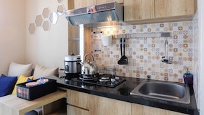 Een kleine keuken met een gasfornuis, waterkoker en moderne apparatuur. Er is een houten kast en een betegelde achterwand.