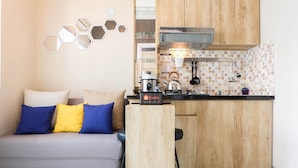 Een knus woongedeelte met een bank, een klein keukenhoekje en een zeshoekige spiegel aan de muur.