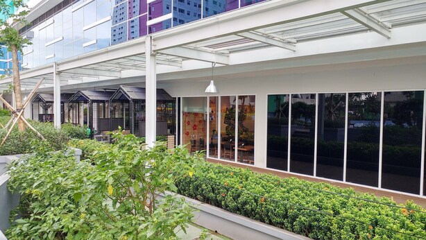 Een modern gebouw met een overdekt terras, grote ramen en groen.