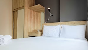 Een keurig opgemaakt bed met witte lakens, een houten hoofdbord en een nachtkastje met een lamp.