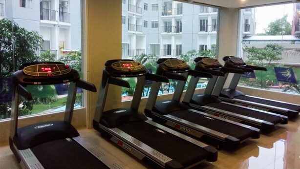 Reihe von Laufbändern in einem Fitnessstudio mit großen Fenstern, die auf einen Wohnbereich blicken.