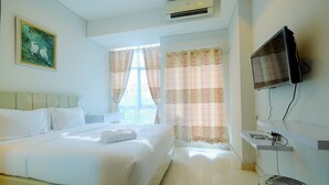Una habitación de hotel con cama, televisor montado, aire acondicionado y un cuadro en la pared.