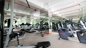 Un gimnasio con varias máquinas de ejercicio, espejos y suelo alfombrado.