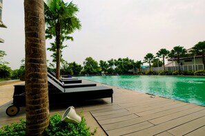A poolside area with lounge chairs and a palm tree. - Best Emerald Studio Room Apartment at Capitol Park Residence (Jakarta)