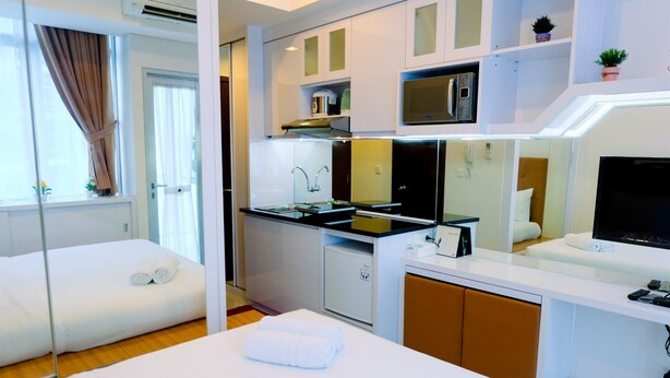 A hotel room with a bed, a small kitchenette, a TV, and a bathroom.