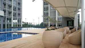 A modern outdoor pool area with a wooden deck, lounge chairs, and a covered seating area. - Comfy Studio Ciputra International Apartment (Jakarta)