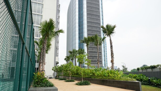 A modern building with a glass facade, surrounded by palm trees and a green fence. - Comfy Studio Ciputra International Apartment (Jakarta)