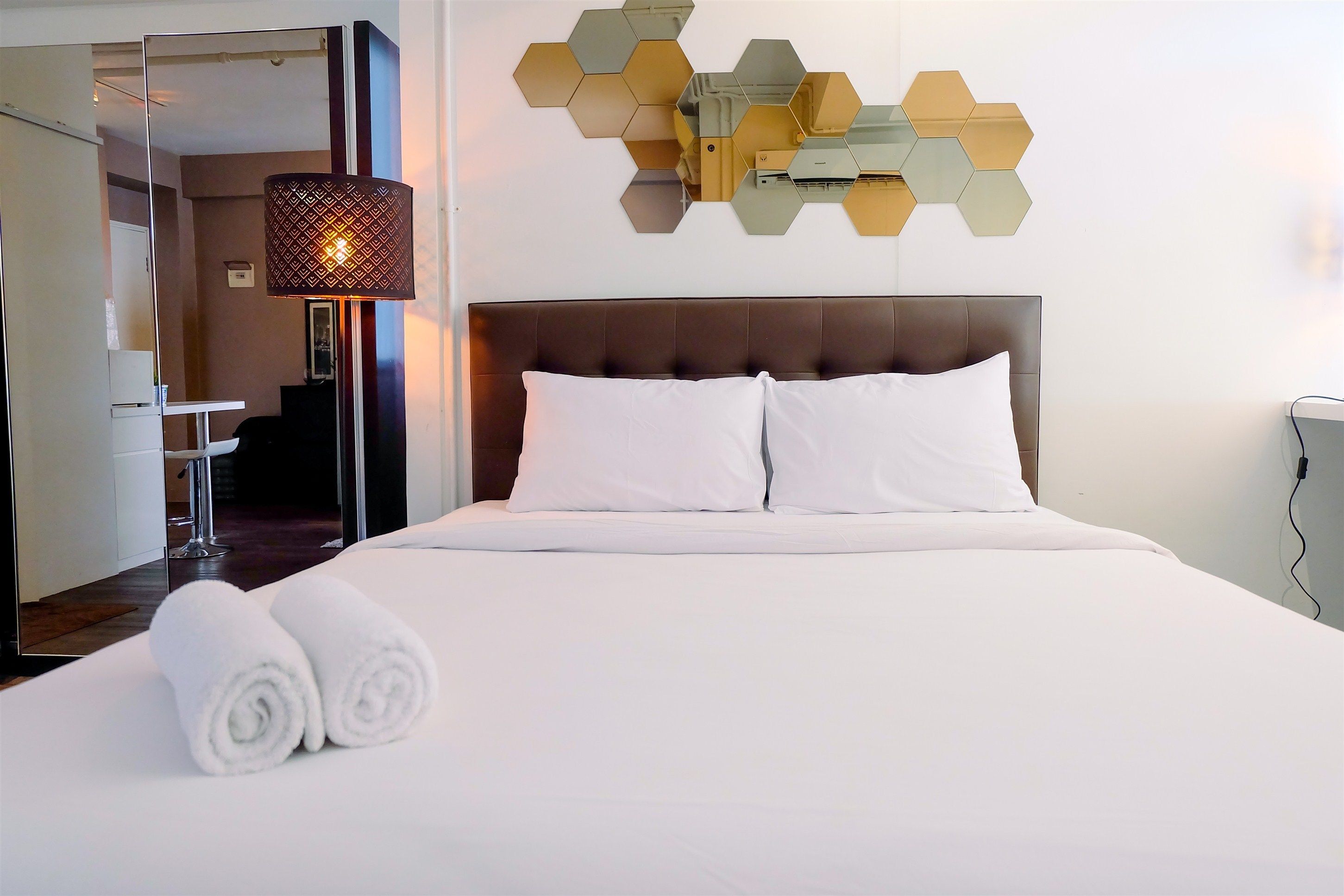 A hotel room with a large bed, white linens, two rolled towels, a modern headboard, and a wall-mounted hexagonal light fixture.