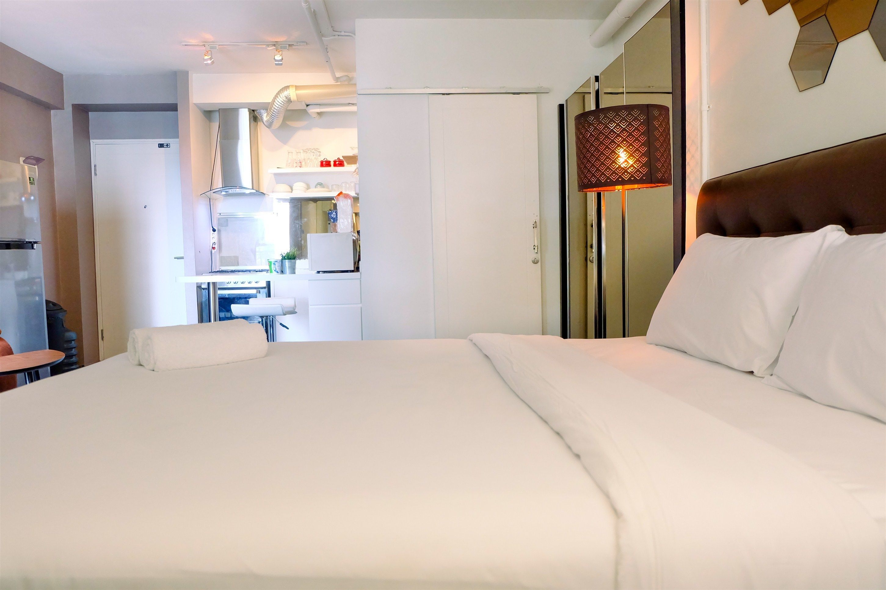 Una habitación de hotel con una cama grande, una lámpara de noche y vistas al área de la cocina.