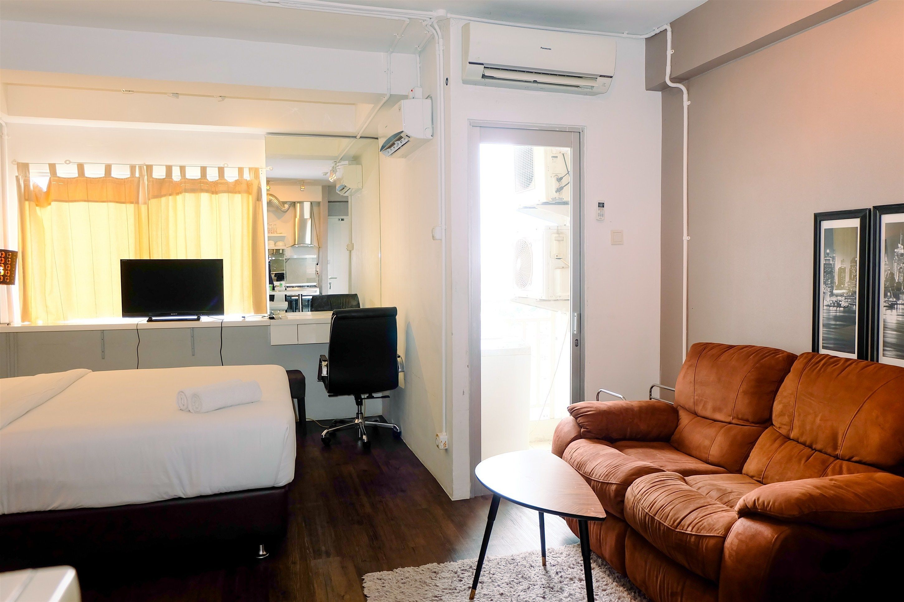 Habitación de hotel con cama, sofá, una mesita, televisor, escritorio y una zona de cocina.