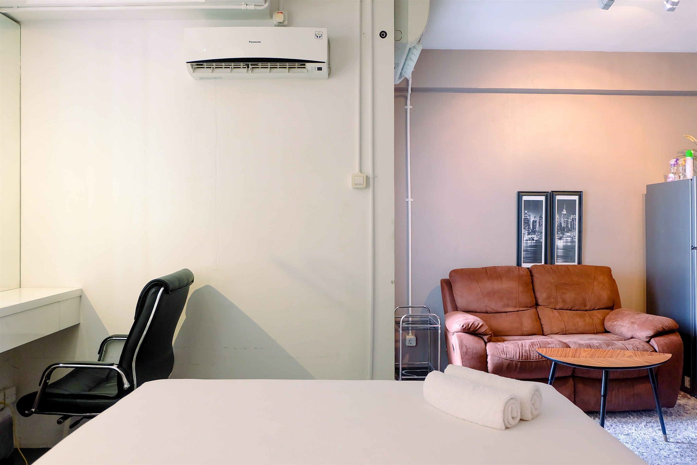 Habitación de hotel con cama, escritorio, silla de oficina negra, sofá de cuero marrón, mesita de madera y toalla blanca sobre la cama.