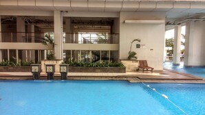 Una piscina interior con agua azul cristalina, rodeada por una solana con baldosas y un área de descanso con una silla.