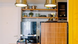 Una cocina compacta con encimera de madera, dos lámparas colgantes, un televisor y una puerta amarilla.