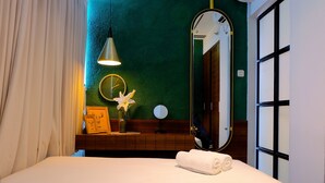 Una cama bien hecha con una toalla enrollada, una mesita de noche con una lámpara, un espejo y un cuadro en la pared.