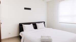 Een netjes opgemaakt bed met wit beddengoed en kussens, een zwart hoofdbord en een raam met zonwering.