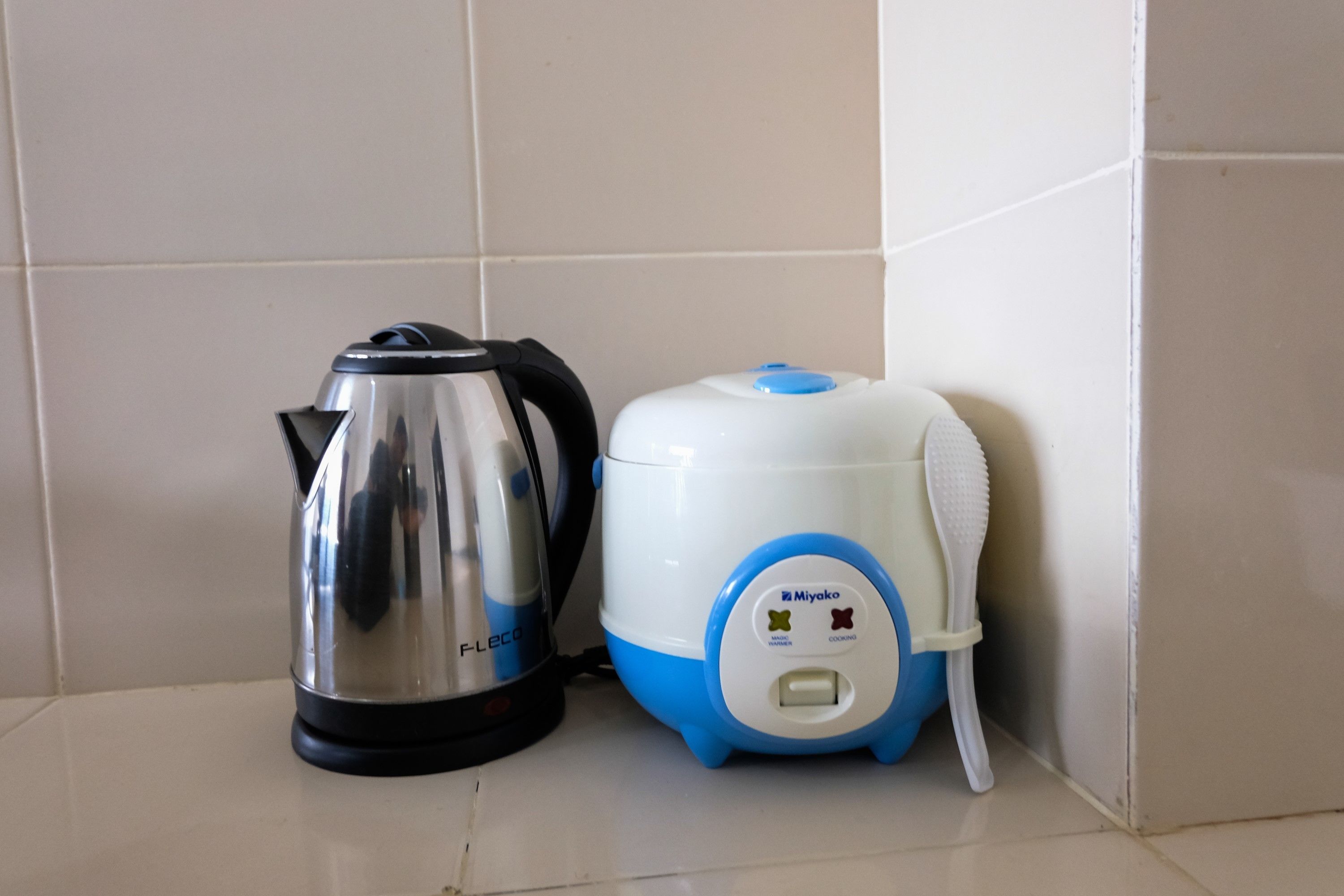 A kitchen area with a stainless steel electric kettle and a white and blue rice cooker.