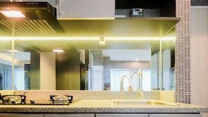 A modern kitchen with a large island, stainless steel appliances, and a large mirror above the sink. - Fabulous Studio Grand Kamala Lagoon Apartment (Bekasi)