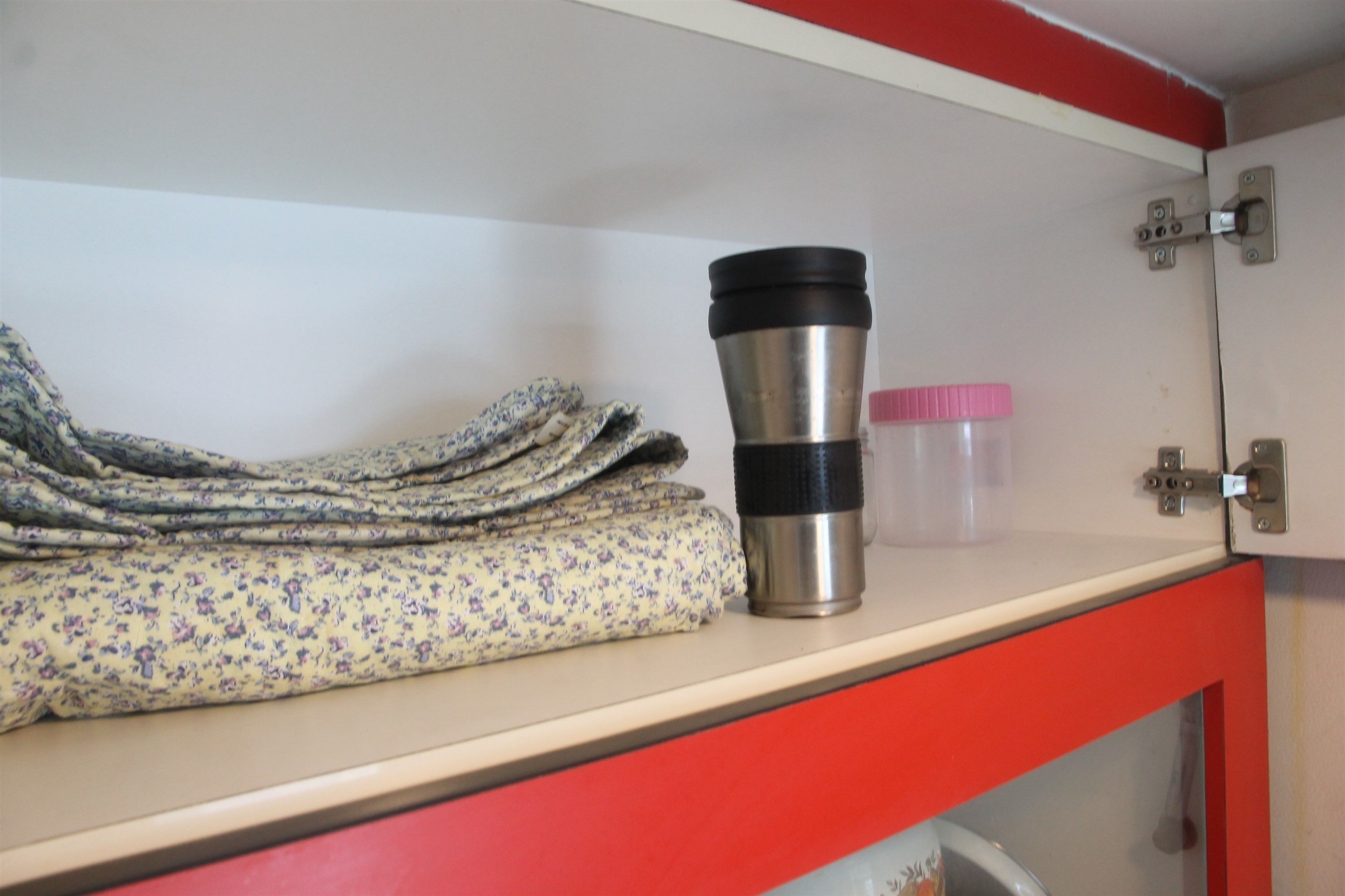 A storage area with a folded towel, a stainless steel thermos, and a plastic container.
