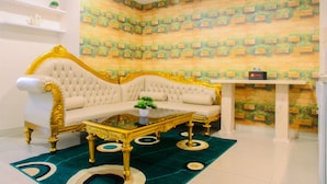 Un salon luxueux avec un canapé blanc et doré, une table basse en verre et un tapis à motifs verts.