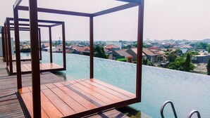 Una terraza de madera con vista a una piscina y una zona residencial al fondo.