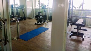 Un gimnasio con equipo de ejercicio, una colchoneta azul y amplias ventanas.