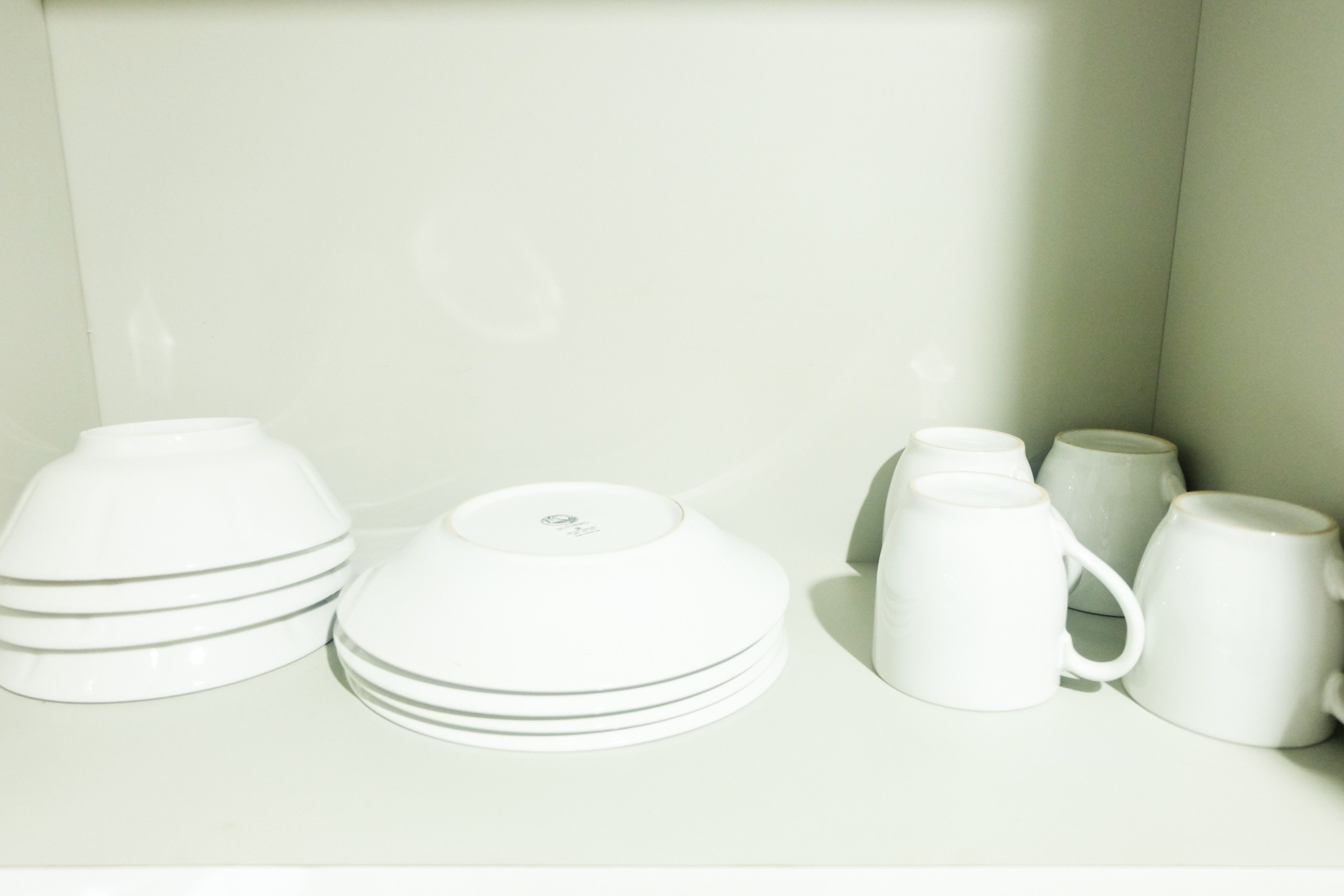 A set of white ceramic dishes and cups arranged on a shelf.