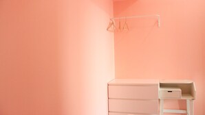 Une pièce avec un mur rose, une commode blanche avec des tiroirs et une étagère blanche.