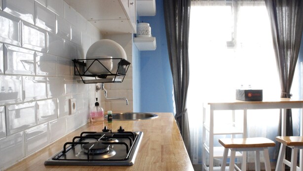 Une cuisine équipée d’une cuisinière à gaz, de meubles blancs, d’un plan de travail en bois, d’un évier et d’une fenêtre avec des rideaux.