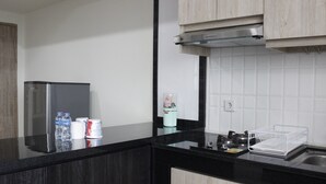 A kitchen with a black countertop, stainless steel refrigerator, and wooden cabinets. - Cozy 2BR Apartment @ Newton Residence (Bandung)