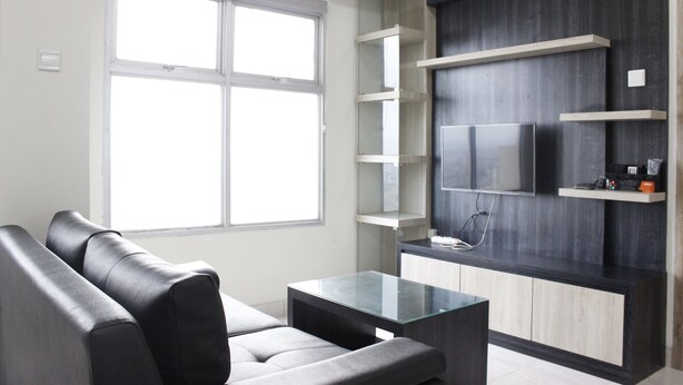 A modern living room with a sofa, a glass coffee table, and built-in shelves. - Cozy 2BR Apartment @ Newton Residence (Bandung)