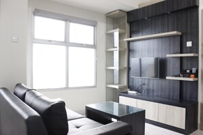 A modern living room with a sofa, a glass coffee table, and built-in shelves. - Cozy 2BR Apartment @ Newton Residence (Bandung)