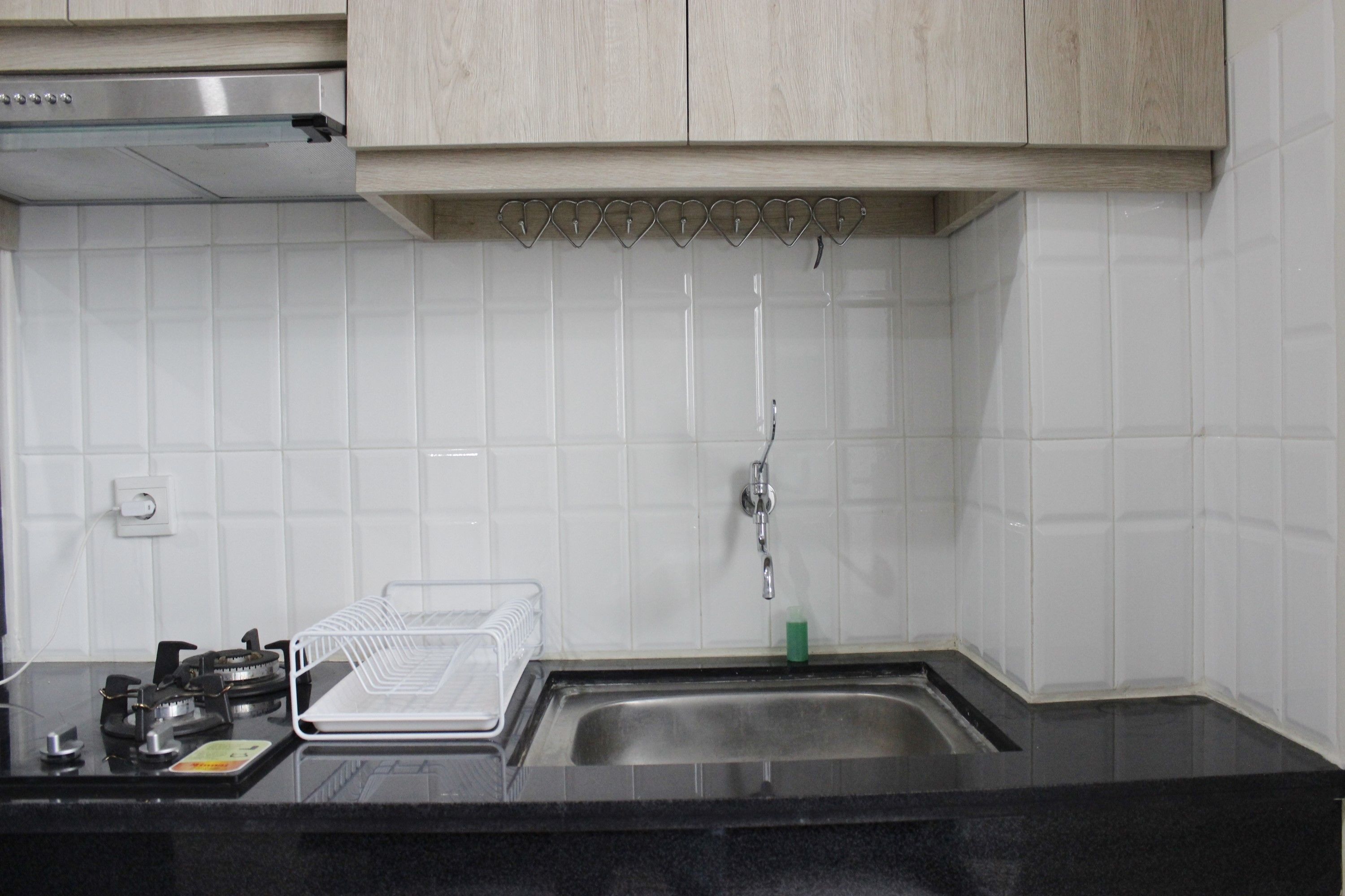 A kitchen with white tiles, a stainless steel sink, a gas stove, and wooden cabinets.